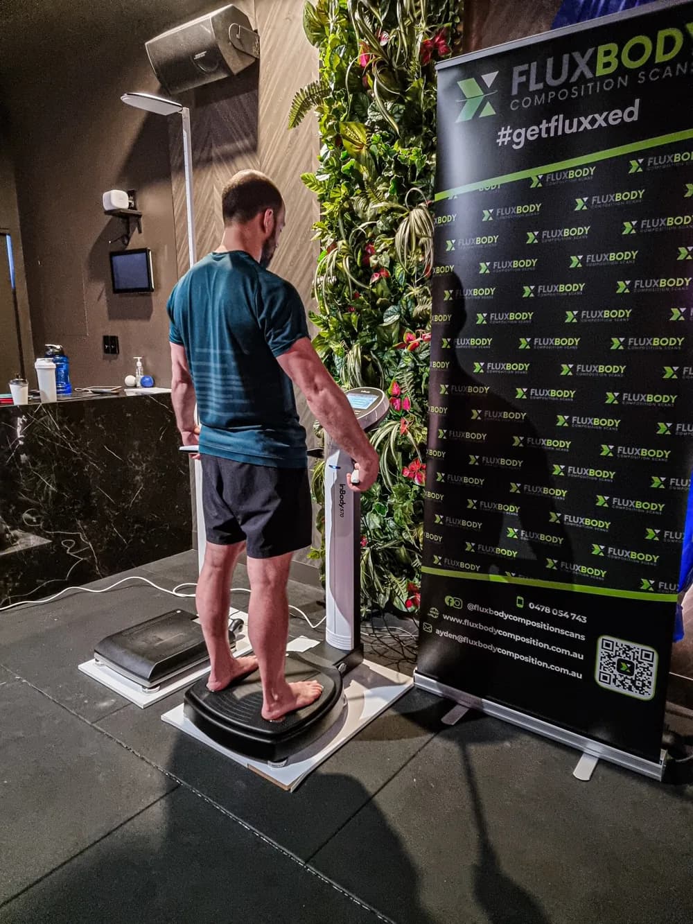 Member being scanned on the InBody570 beside the FluxBody banner at a gym